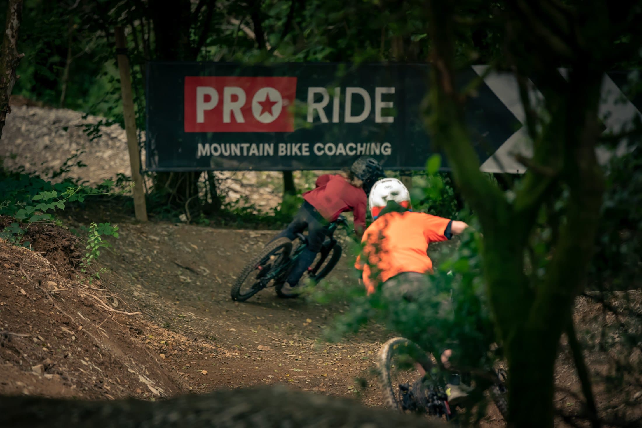 Rider in orange under the Pro Ride Mountain Bike Coaching banner