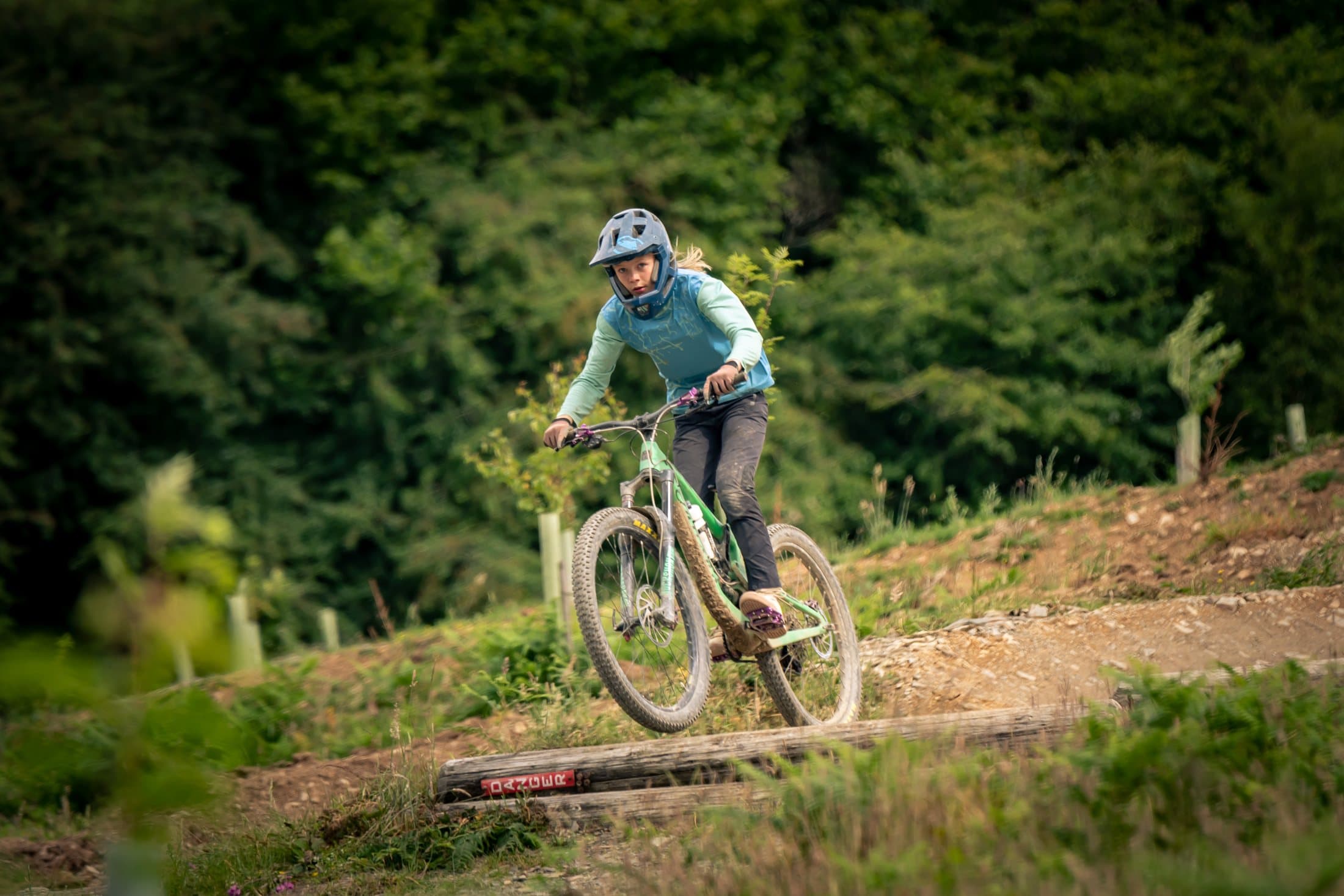 Rider in teal jersey riding a wooden trail feature
