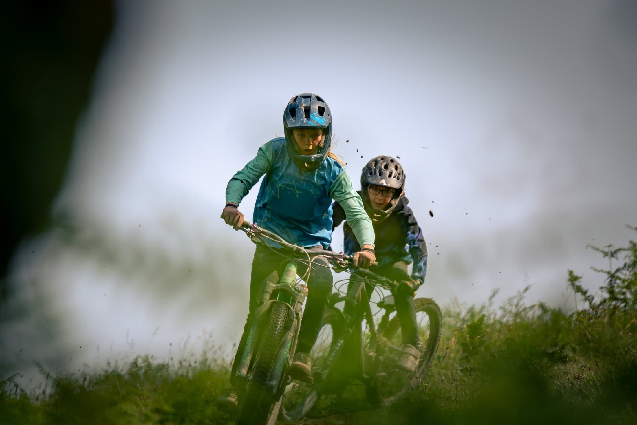 Two riders on a green trail shot through foreground bokeh